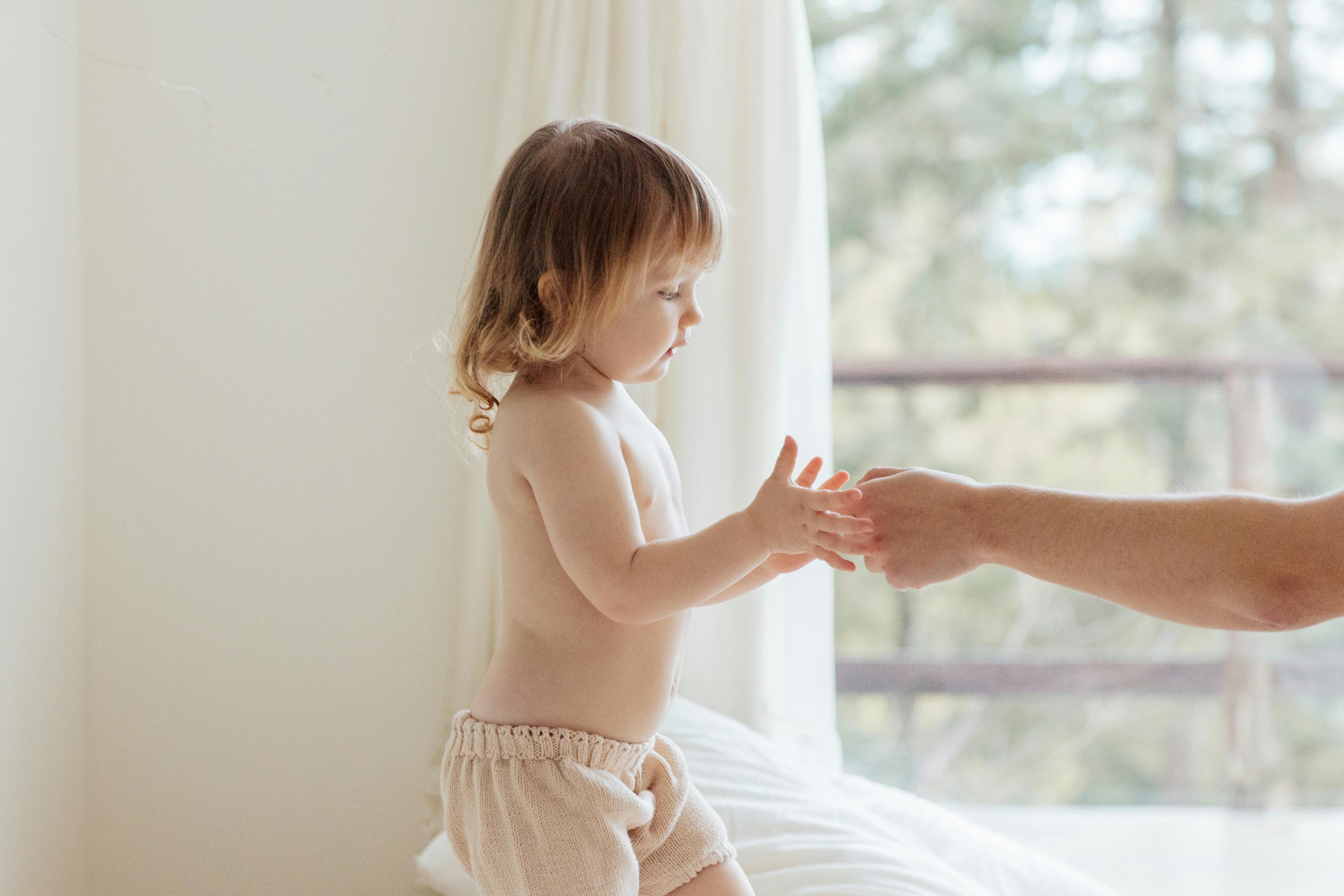 A young child holds hands with an adult in a soft, natural light setting indoors.