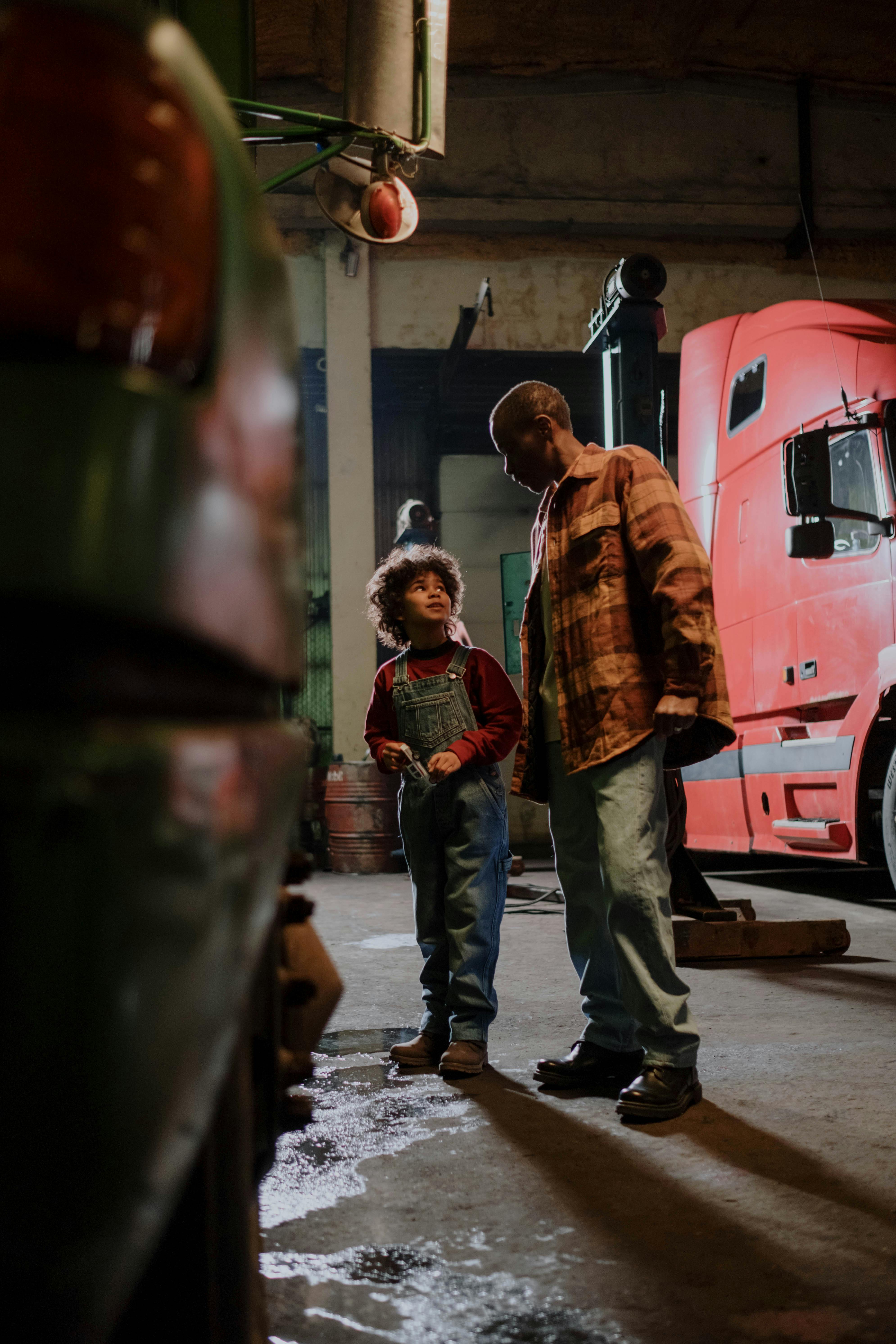 Father and son bonding in a garage with trucks, showcasing family teamwork and learning.