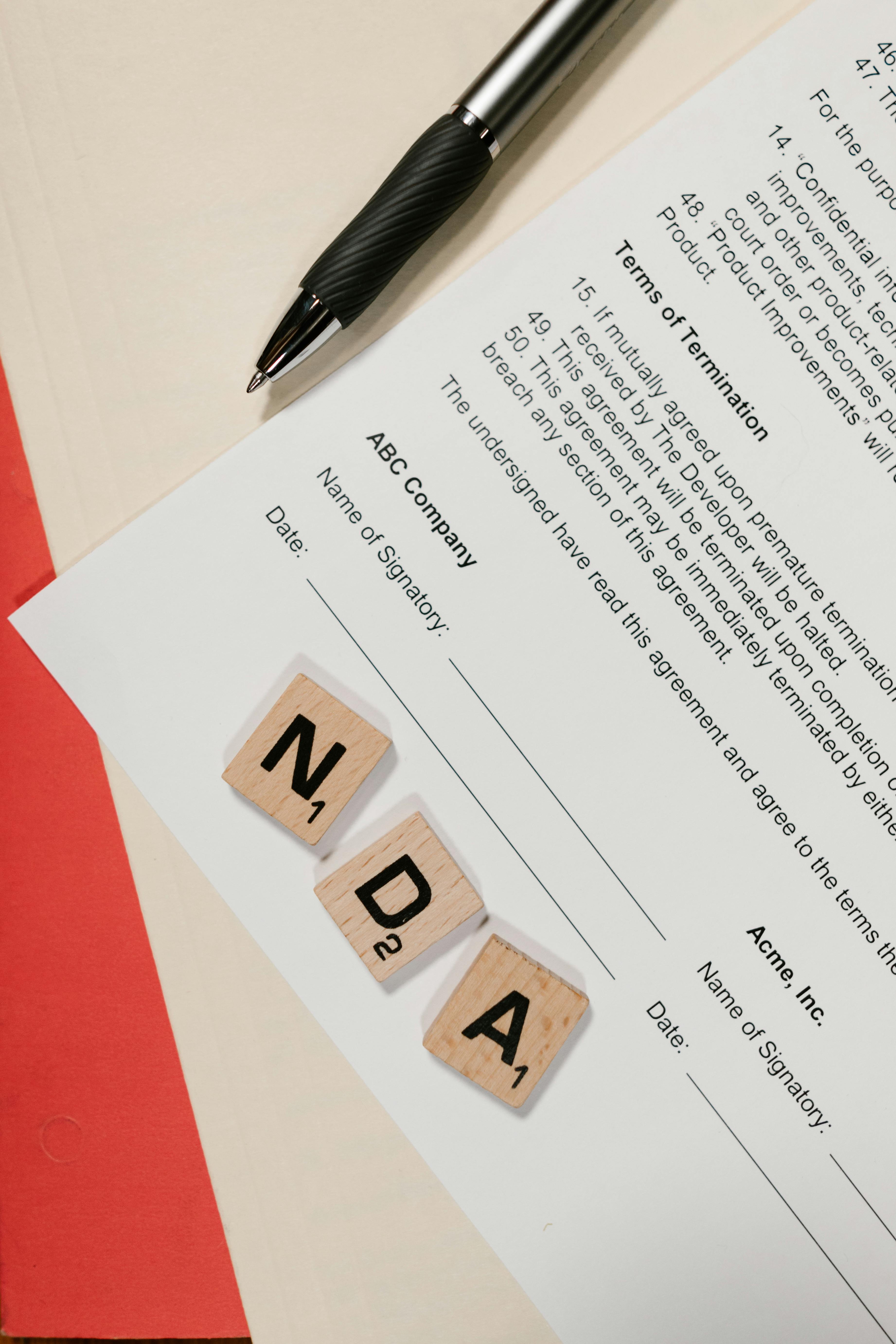 NDA document on table with Scrabble tiles and pen in office setting.